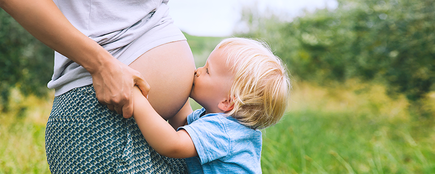 Child Kissing Mother’s Stomach in Natural Setting