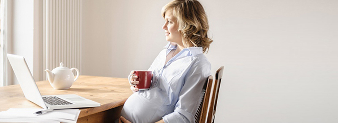 Pregnant woman drinking coffee while on her laptop