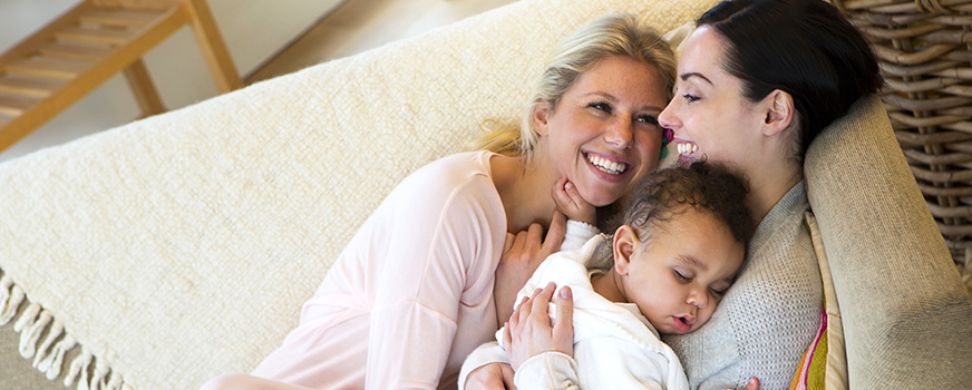 Lesbian Couple Cuddling on Couch with Adopted Baby