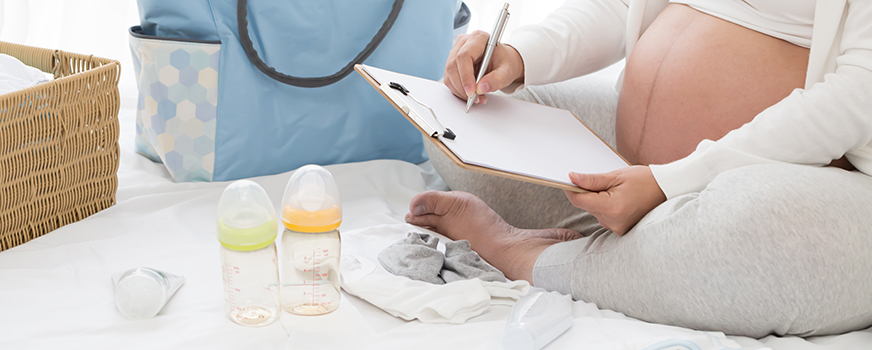 Madre haciendo lista de verificación de bolsas de hospital para artículos de bebé