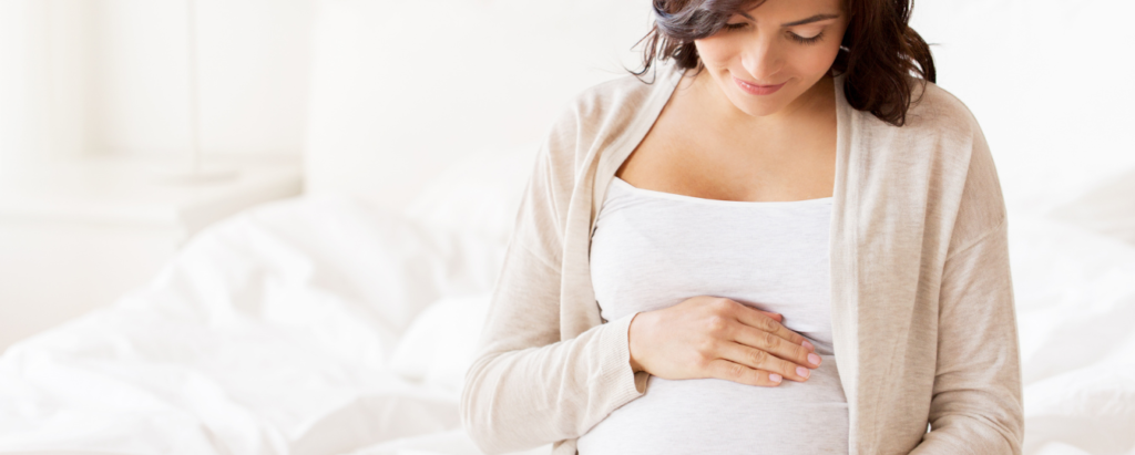 Pregnant Woman Sitting on Bed Holding Belly